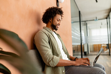 african-american male employee, freelance, programmer typing on laptop in office hallway, positive a