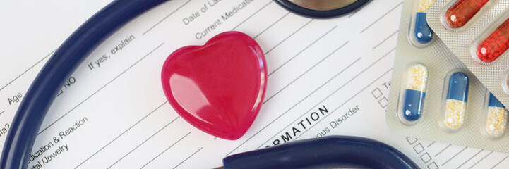 Wall Mural - Red heart with stethoscope and packs of pills on blank medical examination form.