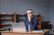 © artmim - Portrait of mature grey haired businessman in glasses and suit sitting by the wooden table and looking on his laptop