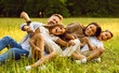 © Studio Romantic - Happy young family of four smiling and having fun while sitting on green grass in park during summer rest. Laughing mother and father hugging their kids boy and girl lying on the field.
