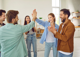 Wall Mural - Portrait of a group of excited happy young friends students greeting each other giving high five when meet at home. Men and women standing in a circle enjoying time together at the party.