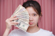 Portrait of asian woman wear white shirt a frown angry and counting holding in hand banknotes or money us dollar exchange money USD on pink background. Business finance and bank employee Concept.