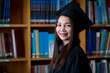 © EduLife Photos - Portrait young happy and excited Asian woman university graduate in graduation gown and cap in the library. Education stock photo