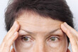 © Марина Демешко - Elderly caucasian worried woman touching the forehead demonstrating wrinkles on her face on a white background. Wrinkling the forehead. Skin care. Beauty concept. Close up. Gymnastics for the face