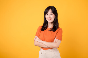 Embrace confidence with a young Asian woman in her 30s, donning an orange shirt, displaying crossed arm sign gesture on yellow background.