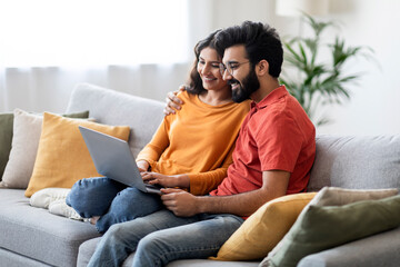 Wall Mural - Millennial Happy Indian Couple Relaxing With Laptop On Couch At Home