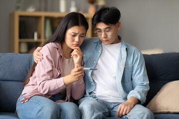 Unhappy Japanese Couple Holding Negative Pregnancy Test Result At Home