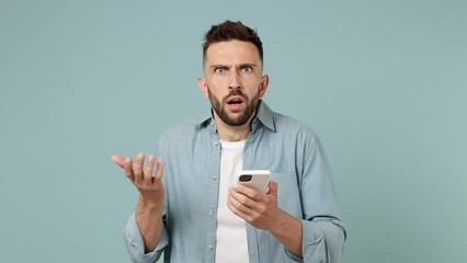 Sad upset young man wear shirt white t-shirt hold use mobile cell phone swear read bad fake news unexpected rumor has some problem isolated on plain pastel light blue cyan background studio portrait