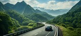 a mountainous, winding road. On a tight lane, there are two cars approaching each other to pass. a lush forest surrounds you.