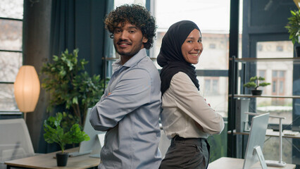 Two happy business partners diverse multiracial colleagues managers entrepreneurs Muslim businesswoman in hijab and Indian latino businessman in corporate office posing crossed hands team partnership