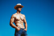 Handsome young man with a perfect body posing in cowboy hat and jeans in the field. Outdoor shot