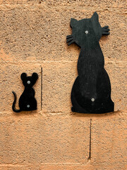 a cat and a black wooden mouse decorate an orange cement wall, a funny cat and a mouse sitting side by side, vertical