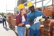 © JackF - African-american man and European woman standing and talking beside clay brick stacks in outdoor construction material storage. They're discussing documentation.