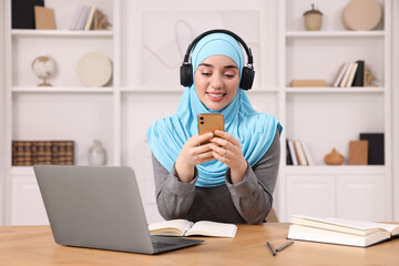 Poster - Muslim woman using smartphone near laptop at wooden table in room