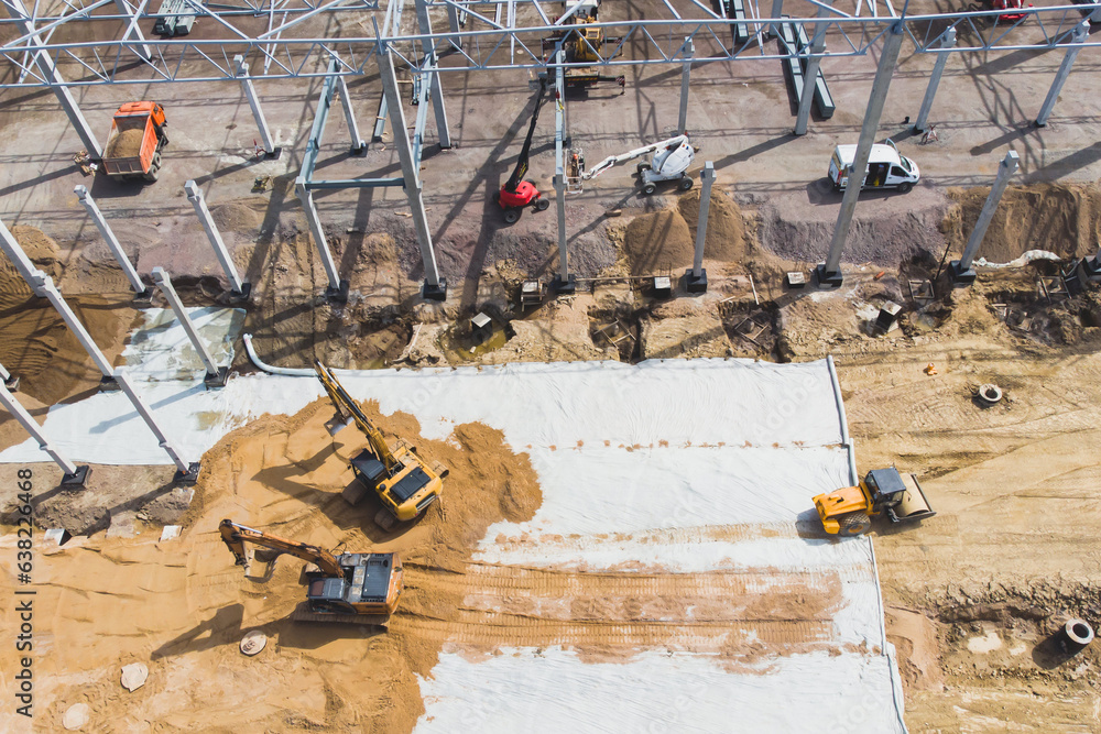 Construction site of a large warehouse storage building and logistics center, heavy vehicle working, excavator, crane, truck and bulldozer, steel frame structure of modern factory hangar, aerial view