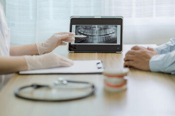 Female dentist wearing rubber gloves examining dental health of her male patient at clinic using dental implants to guide treatment and x-ray visualization on tablet, oral health care concept