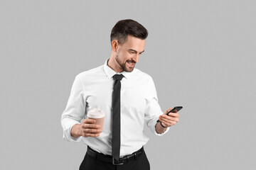 Poster - Handsome businessman with cup of coffee and mobile phone on grey background