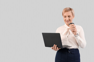 Wall Mural - Mature businesswoman with laptop and coffee on grey background