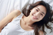 © Surachetsh - Pretty Asian young lady lies on indoor bed. She keeps eyes open and looks satisfied with positive thinking and smiling to camera. Generative AI.