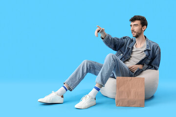 Wall Mural - Handsome young man with mobile phone pointing at something on blue background