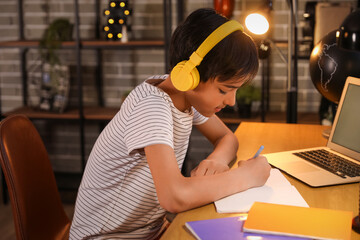 Wall Mural - Little boy with headphones studying at home late in evening