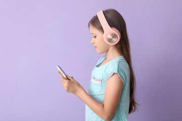 Sticker - Little girl in headphones using mobile phone on lilac background