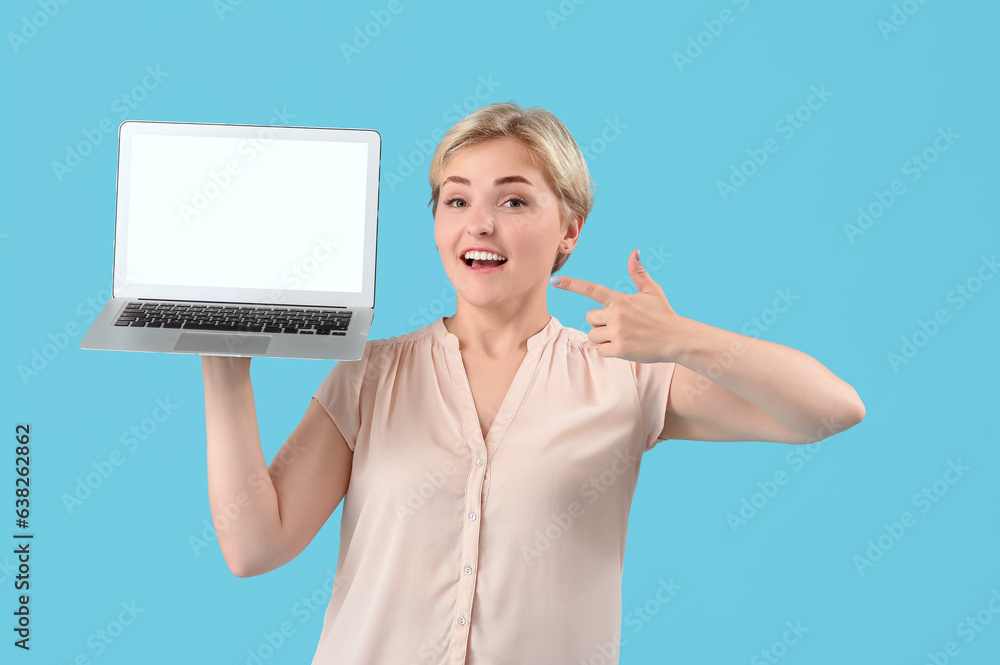 Happy young female programmer pointing at laptop on blue background