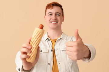 Sticker - Young man with tasty hot dog showing thumb-up gesture on beige background