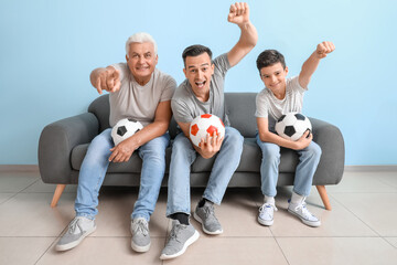 Wall Mural - Little boy with his dad and grandfather watching football game near blue wall