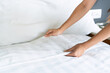 © Pattarisara - Close up of maid hands set up white bed sheet in hotel room, copy space for text