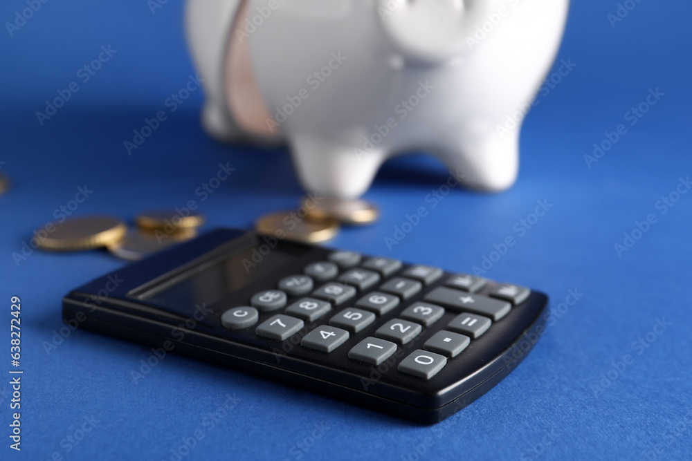 Broken piggy bank with coins and calculator on blue background