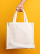 Person holding a tote bag, white canvas shopping bag with no label or print, blank tote in front of yellow background, good for mock-up
