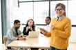 © bongkarn - A smiling Asian businesswoman in glasses standing with a tablet in her hand in a meeting room