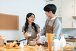 © bongkarn - A joyful Asian couple enjoys baking pastry or making pancakes in the kitchen together.