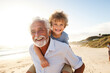 Happy grandfather joyfully piggybacking his cute little grandson on the beach