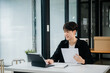 © laddawan - Confident Asian man with a smile standing holding notepad and tablet at the office.