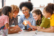 Multiethnic teacher and kids studying electricity and incandescent light bulb at physics lesson.