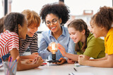 Fototapeta Panele - Multiethnic teacher and kids studying electricity and incandescent light bulb at physics lesson.