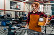© DusanJelicic - Woman with curly red hair standing in workshop, holding protective equipment under arm and smiling at camera, workshop in background