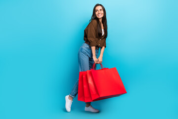 Sticker - Full body length cadre of dreamy young fashionista woman holding red packages bargains sale purchase ad isolated on blue color background