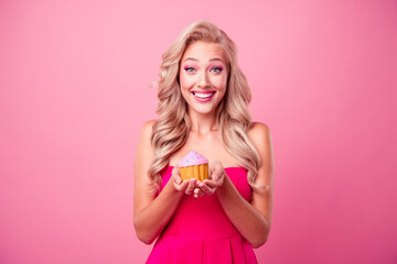 Poster - Portrait of adorable cheerful girl toothy smile hands hold little tasty cake muffin isolated on pink color background