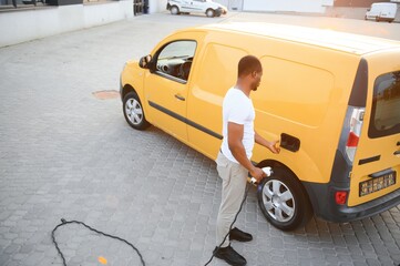 Wall Mural - African american Man stands next to electric delivery vans at electric vehicle charging station