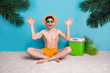 Canvas Print - Full length photo of cute excited guy swimwear sunhat sitting beach rising hands arms isolated blue color background