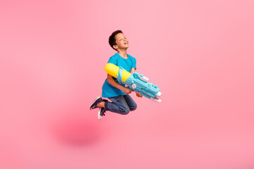 full length photo of cool positive little boy dressed blue t-shirt jumping high shooting water gun i