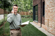 © LIGHTFIELD STUDIOS - cheerful real estate broker with folder talking on smartphone and looking at camera near house