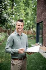 Wall Mural - overjoyed property broker looking at camera while standing with folder and pen near cottage