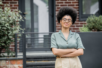 Wall Mural - confident african american real estate agent in eyeglasses looking at camera outdoors