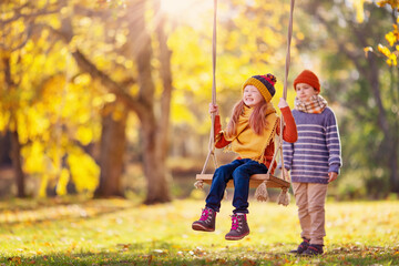 Wall Mural - Boy swinging smiling girl on the rope swing in the autumnal park.