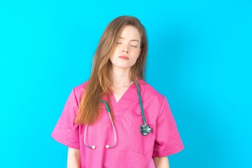beautiful doctor woman standing over blue studio background  looking sleepy and tired, exhausted for fatigue and hangover, lazy eyes in the morning.