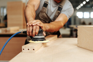 Close up of carpenter hands sanding wood with orbital sander at workshop